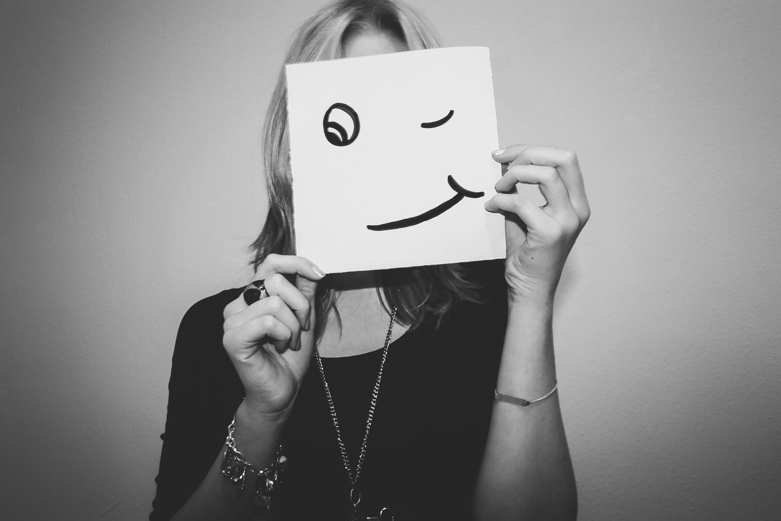Stock image of a person holding a sign with a smiley face on it over their face.